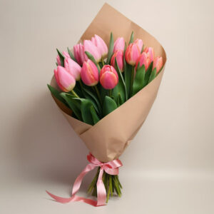 A Tulip Garden of pink tulips wrapped in brown paper and tied with a pink ribbon, set against a light beige background.